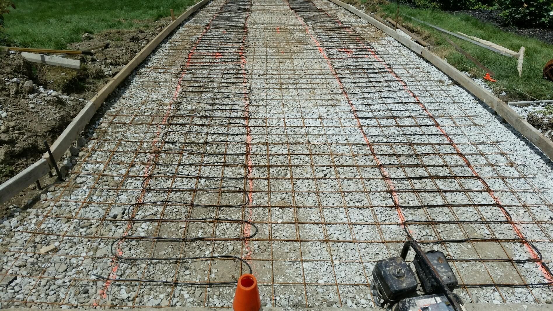 Rebar grid laid over a concrete road foundation under construction, with gravel shoulders and grass edges