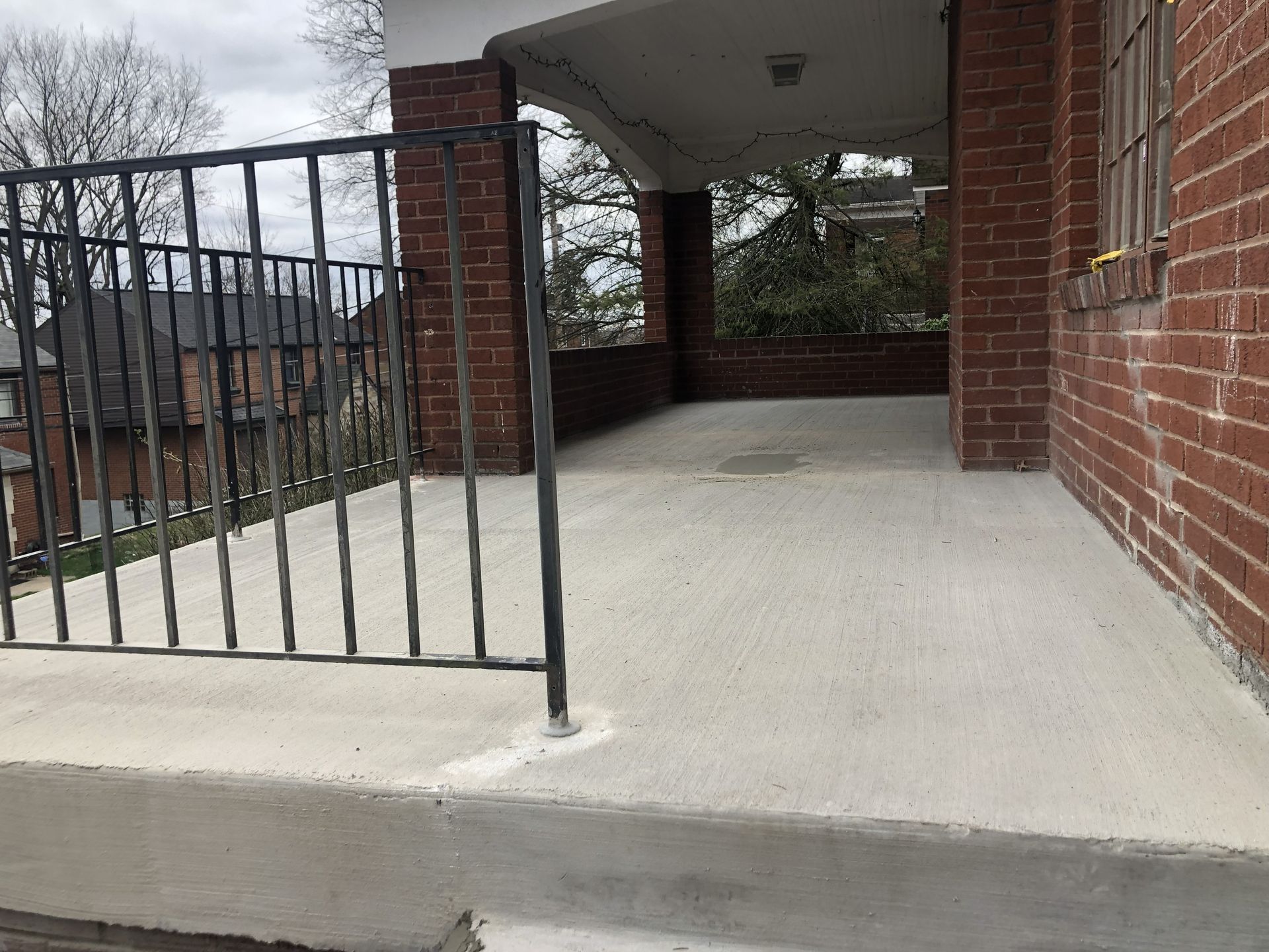 Brick porch with concrete floor and black metal railing at a house entrance