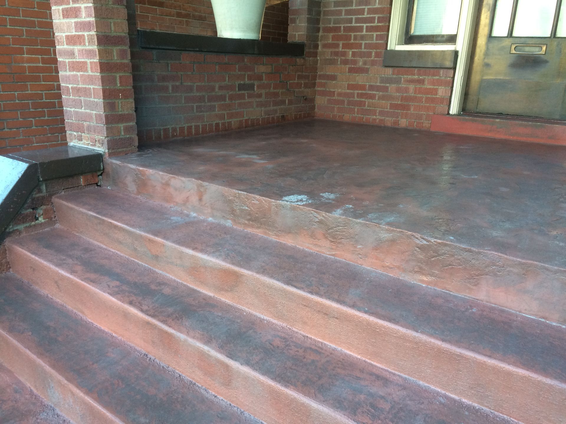 Brick porch with four red concrete steps leading to a covered entryway and wooden door.