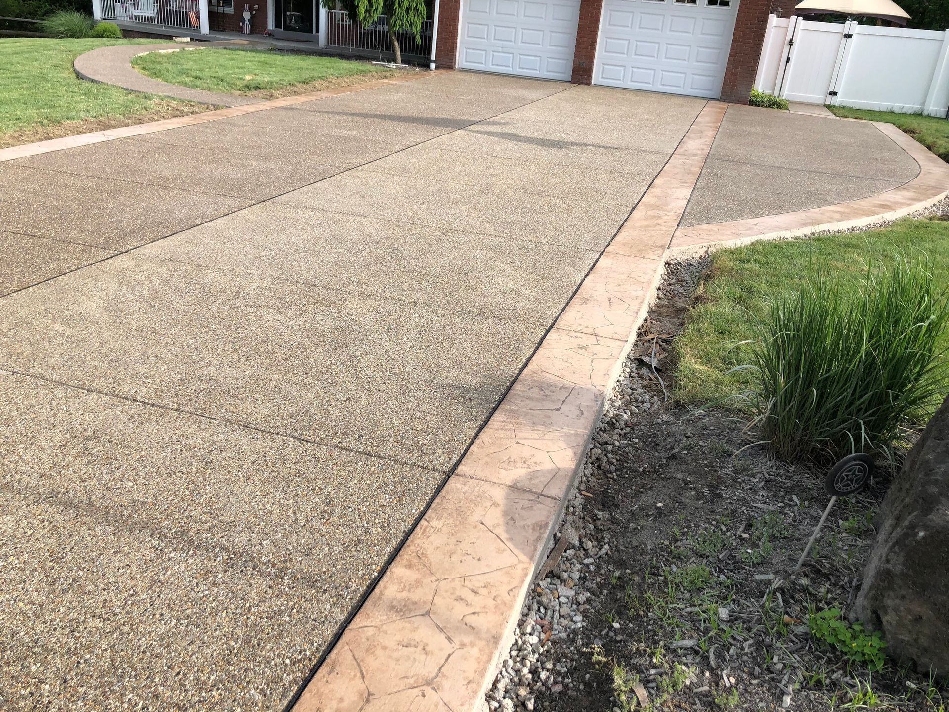 Residential driveway with textured concrete and a curved brick border leading to a garage.