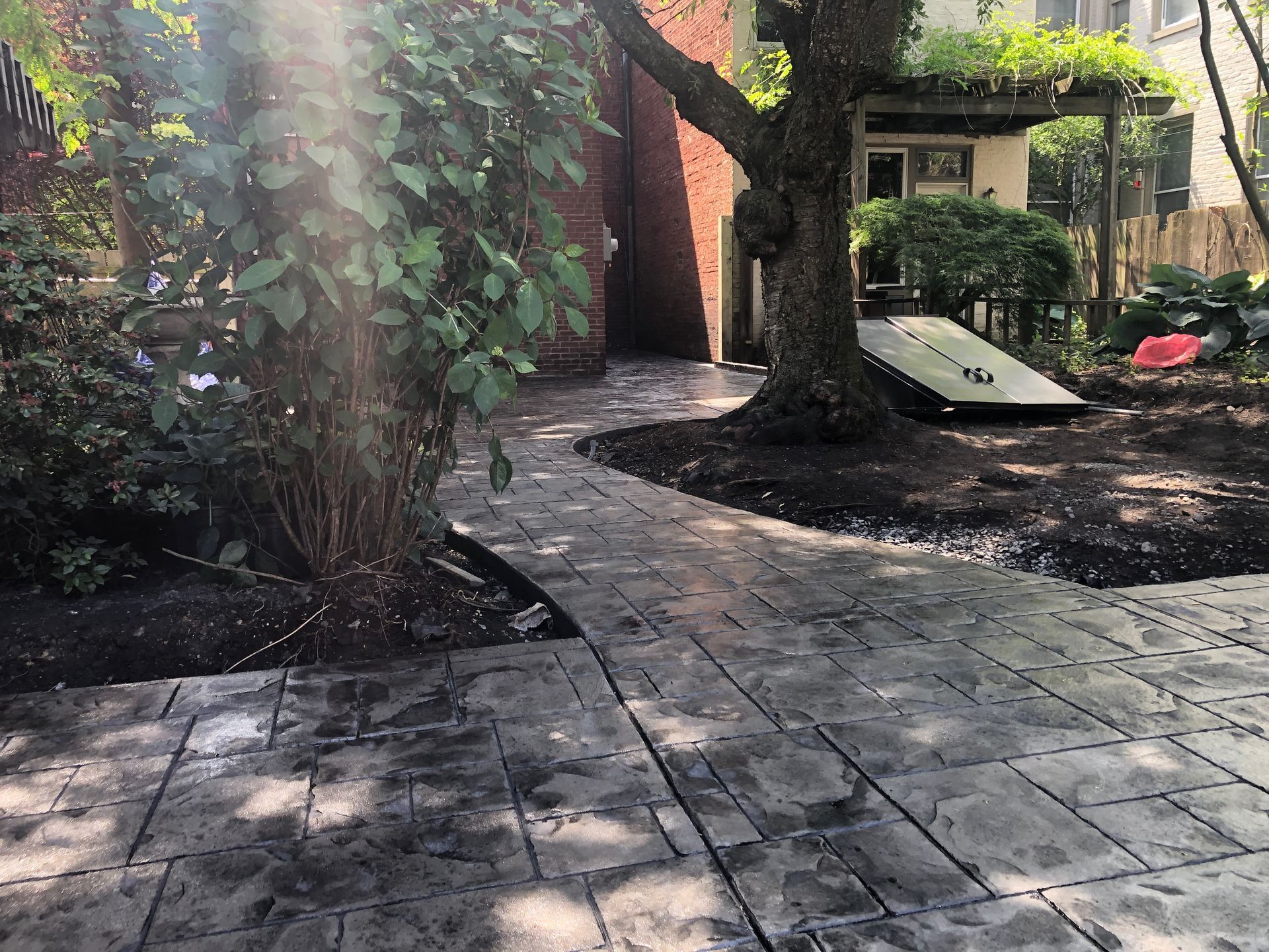 Tree-lined courtyard with stone path, brick wall, and a small playground slide and play structure.