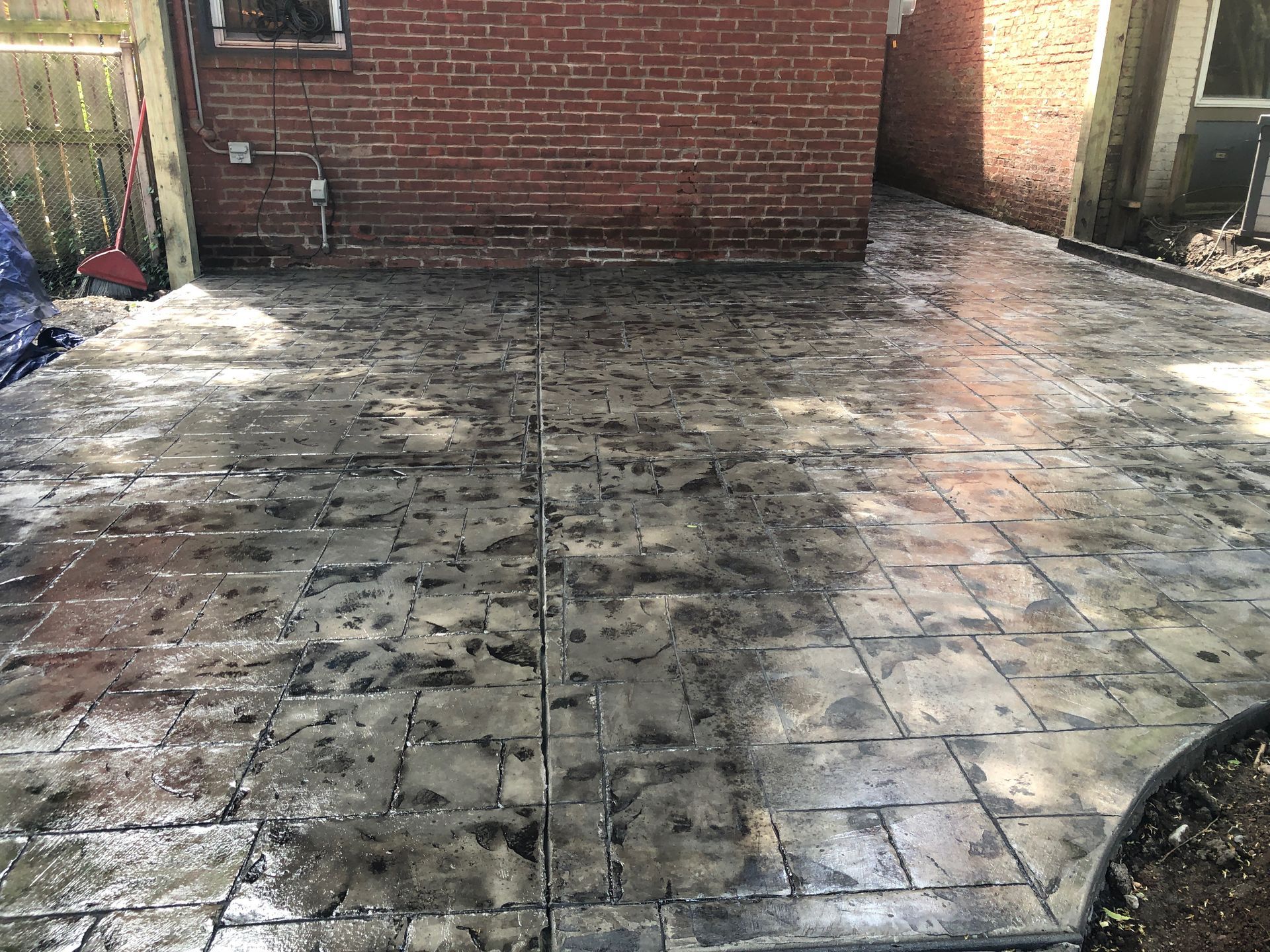 Wet, muddy backyard patio with tiled paving and brick walls.