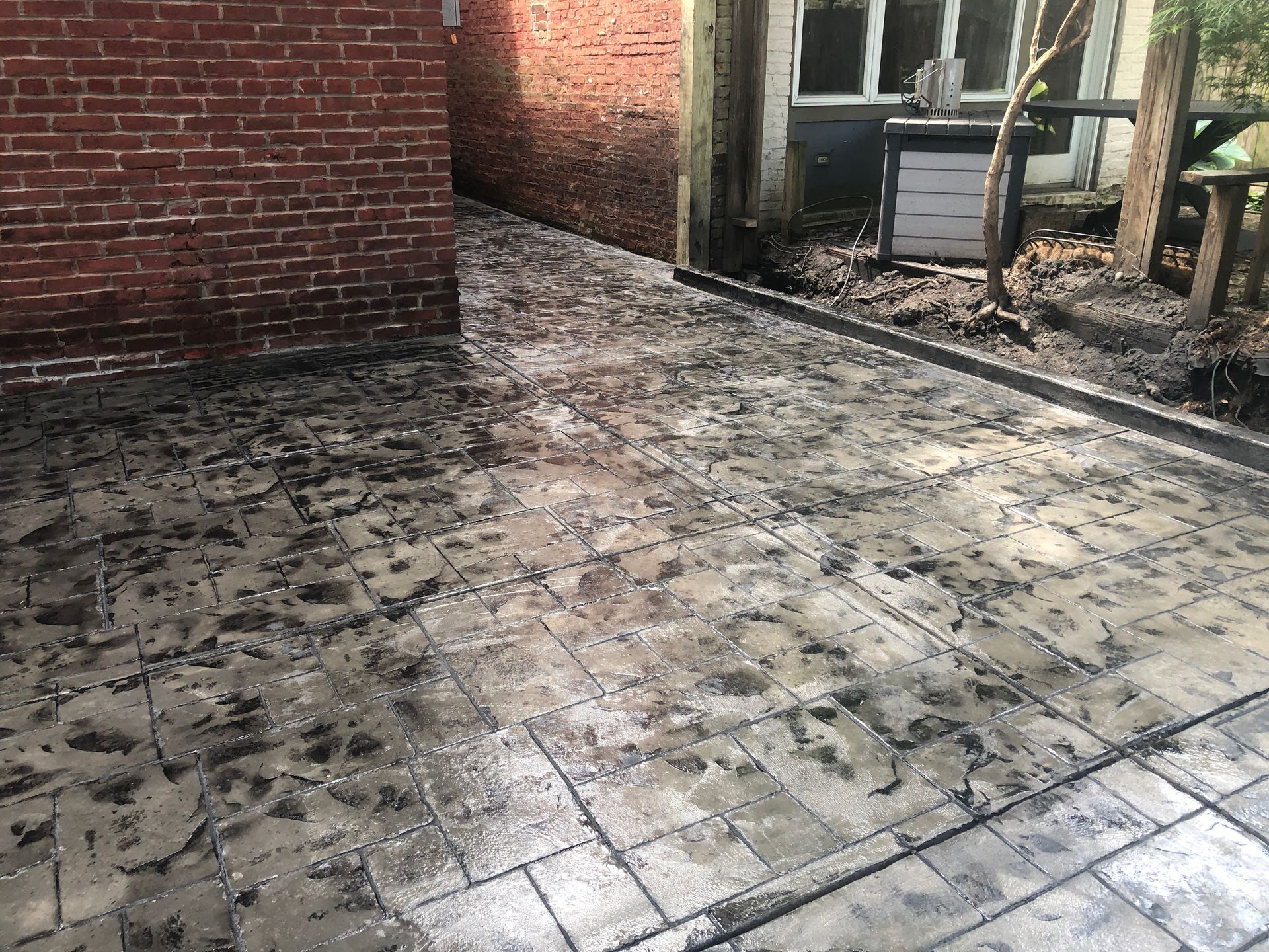 Dirty tiled patio beside brick walls and a fence, with muddy debris scattered across the ground.