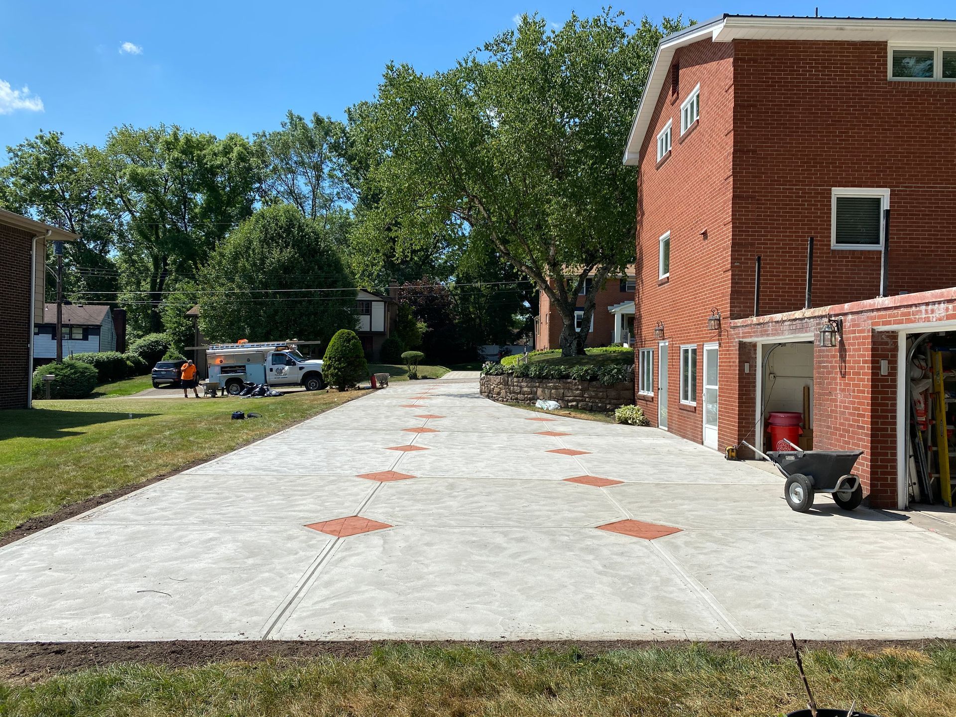Concrete driveway beside a red brick apartment building, with orange markings and trees under a clear blue sky