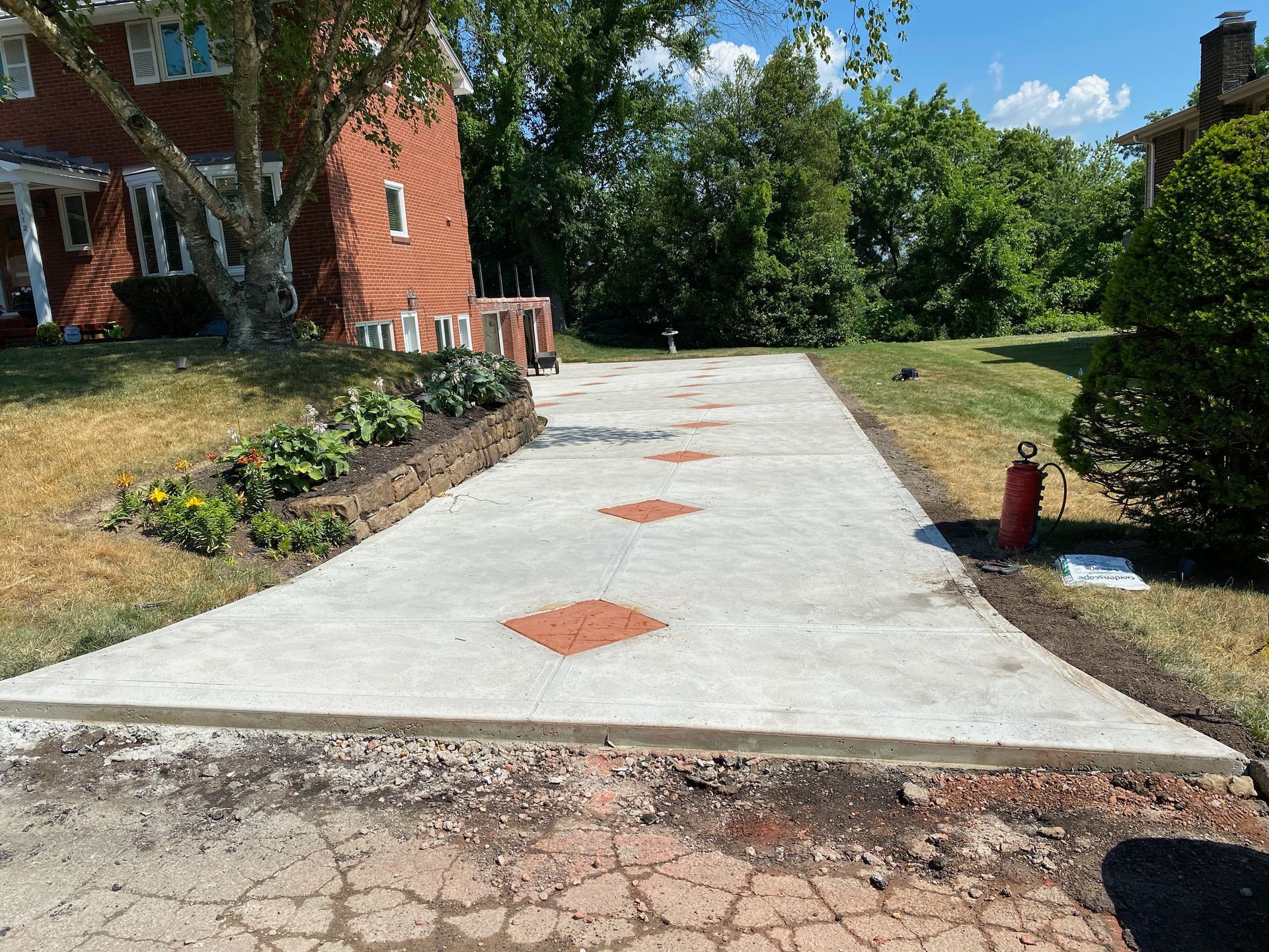 Concrete driveway with orange square markers leading to a brick house, bordered by grass and shrubs.