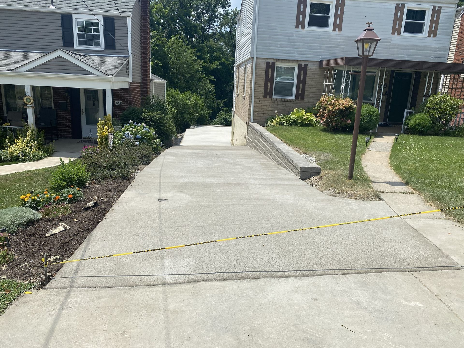 Concrete driveway ramp between suburban houses, with yellow tape across it and a streetlamp on the right.