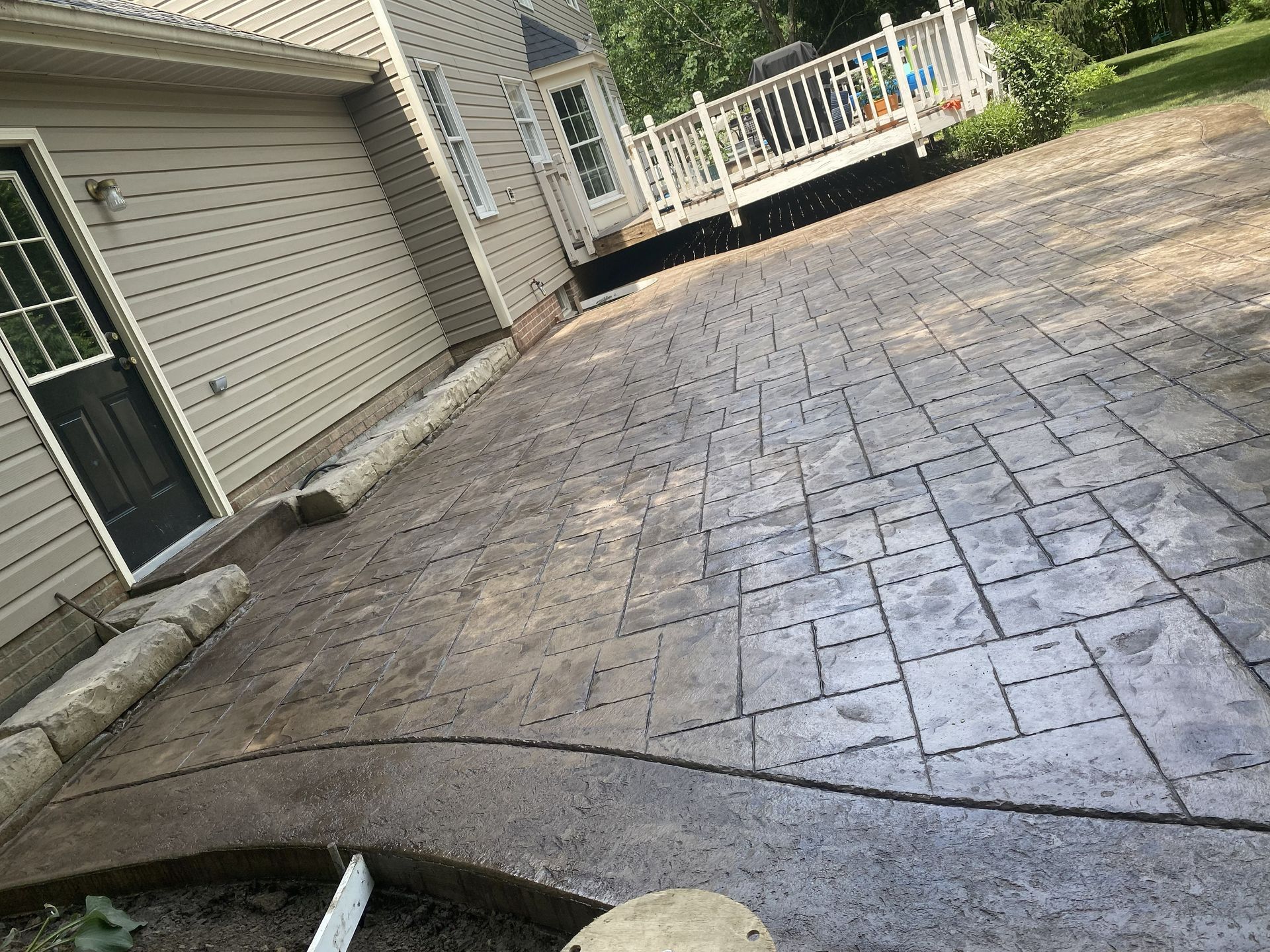 Stamped concrete driveway beside a garage and porch, viewed at an angle with a curved planter edge in foreground