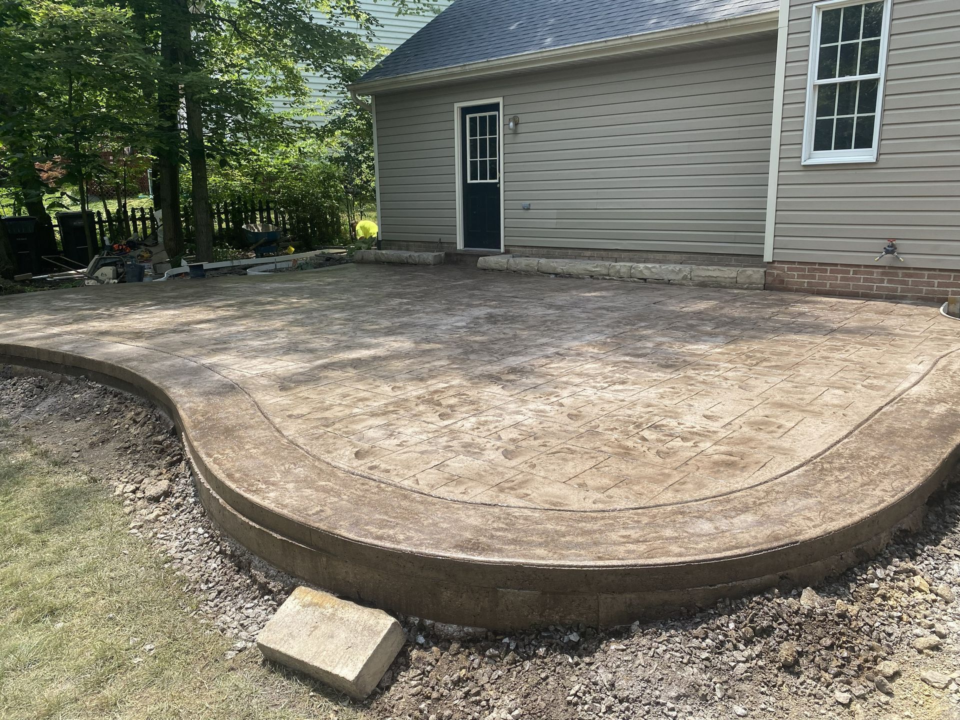 Curved concrete patio beside a house with a dark door and wooded yard