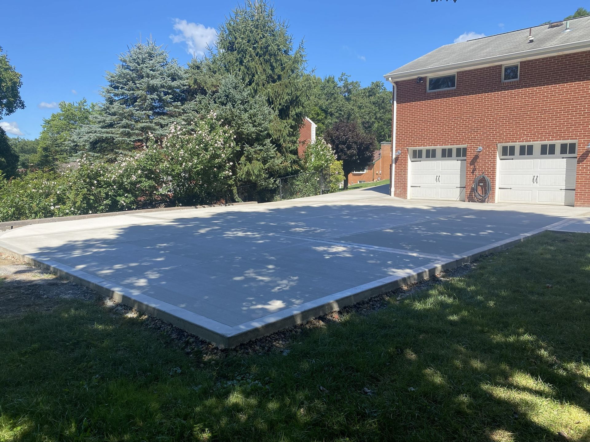 Concrete driveway beside a brick garage and grassy yard on a sunny day