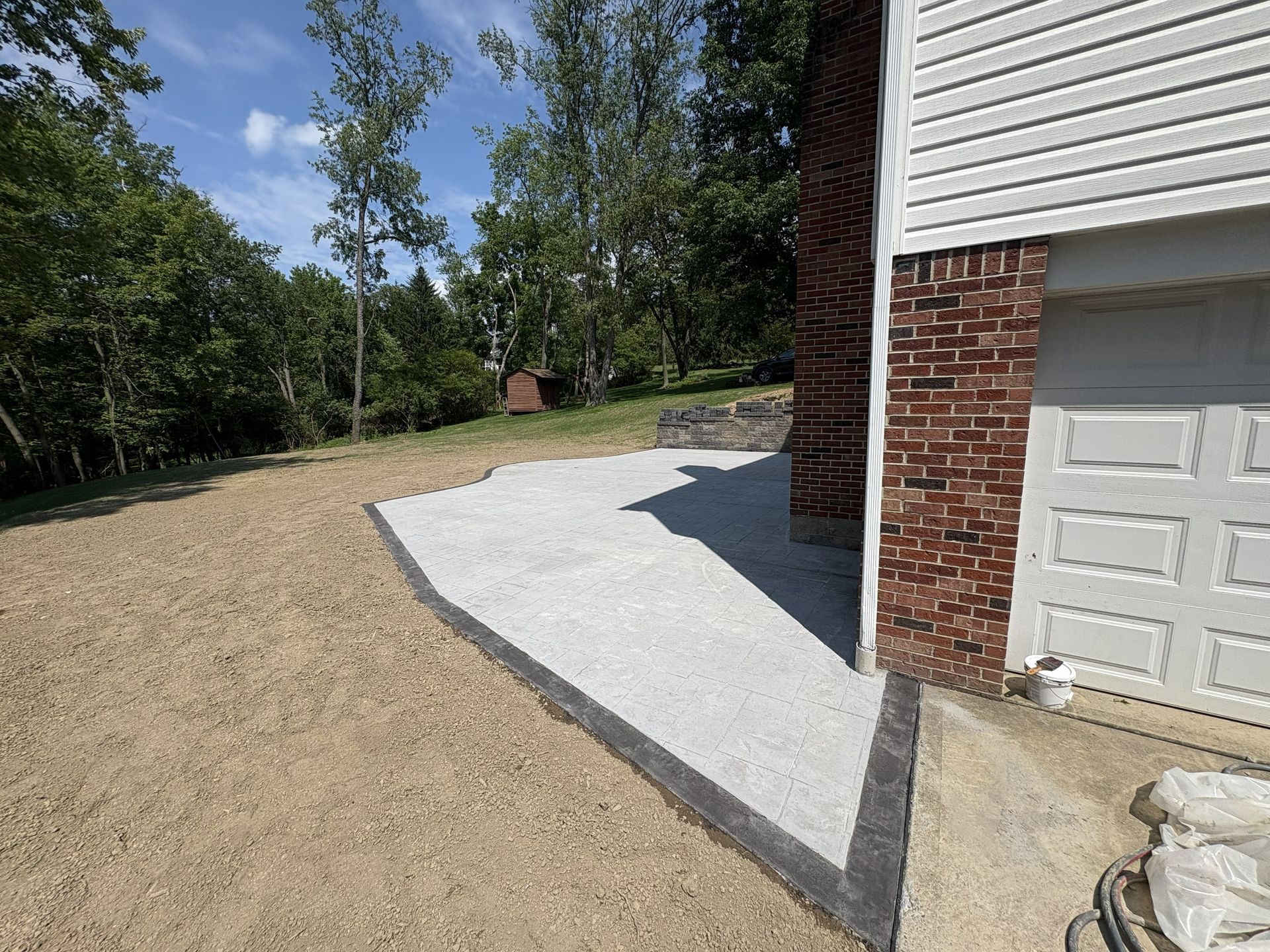 Gravel driveway beside a brick house, with a white concrete pad and garage door on the right.