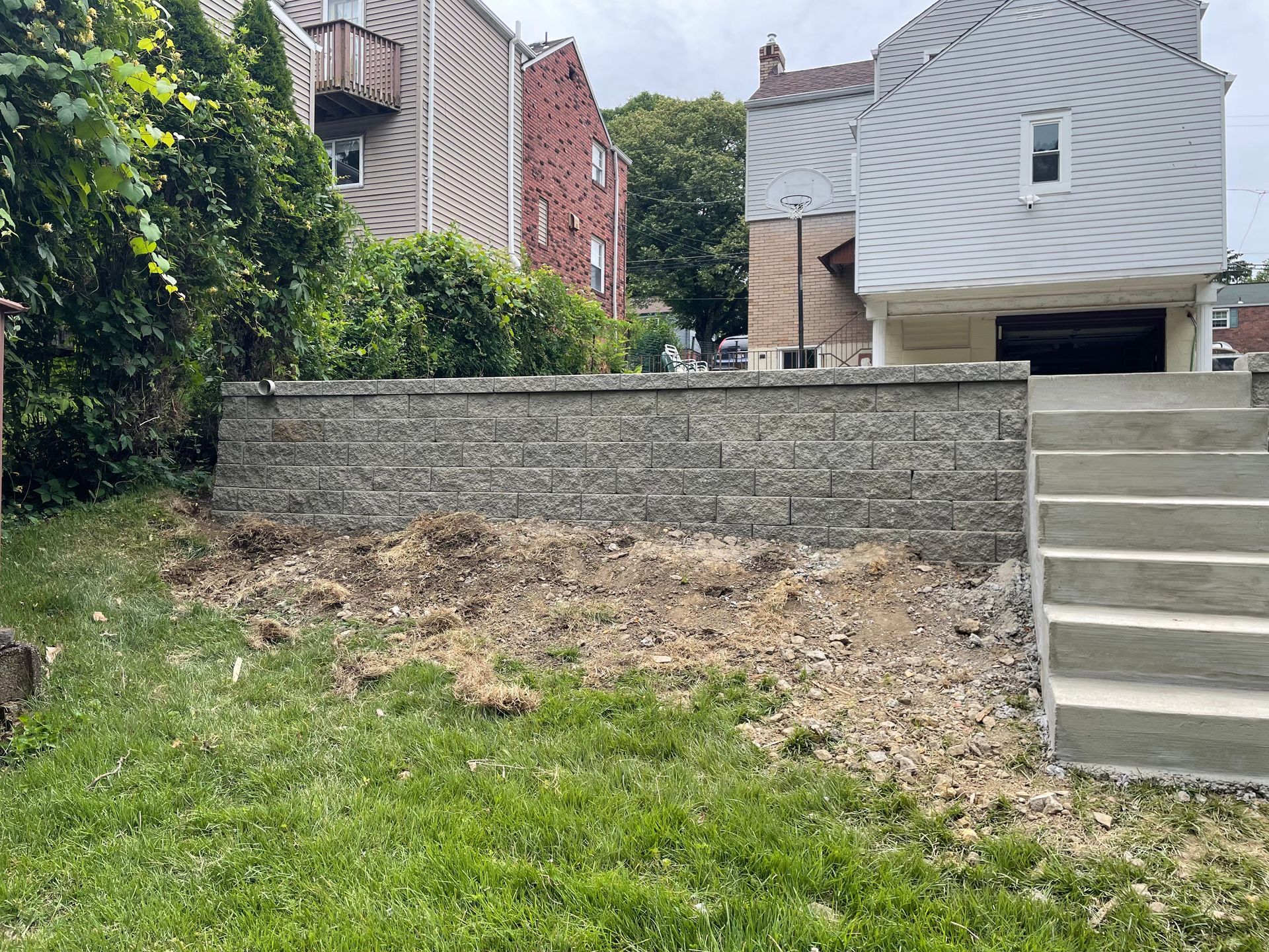 Backyard with a concrete retaining wall, grassy slope, and exterior stairs beside houses