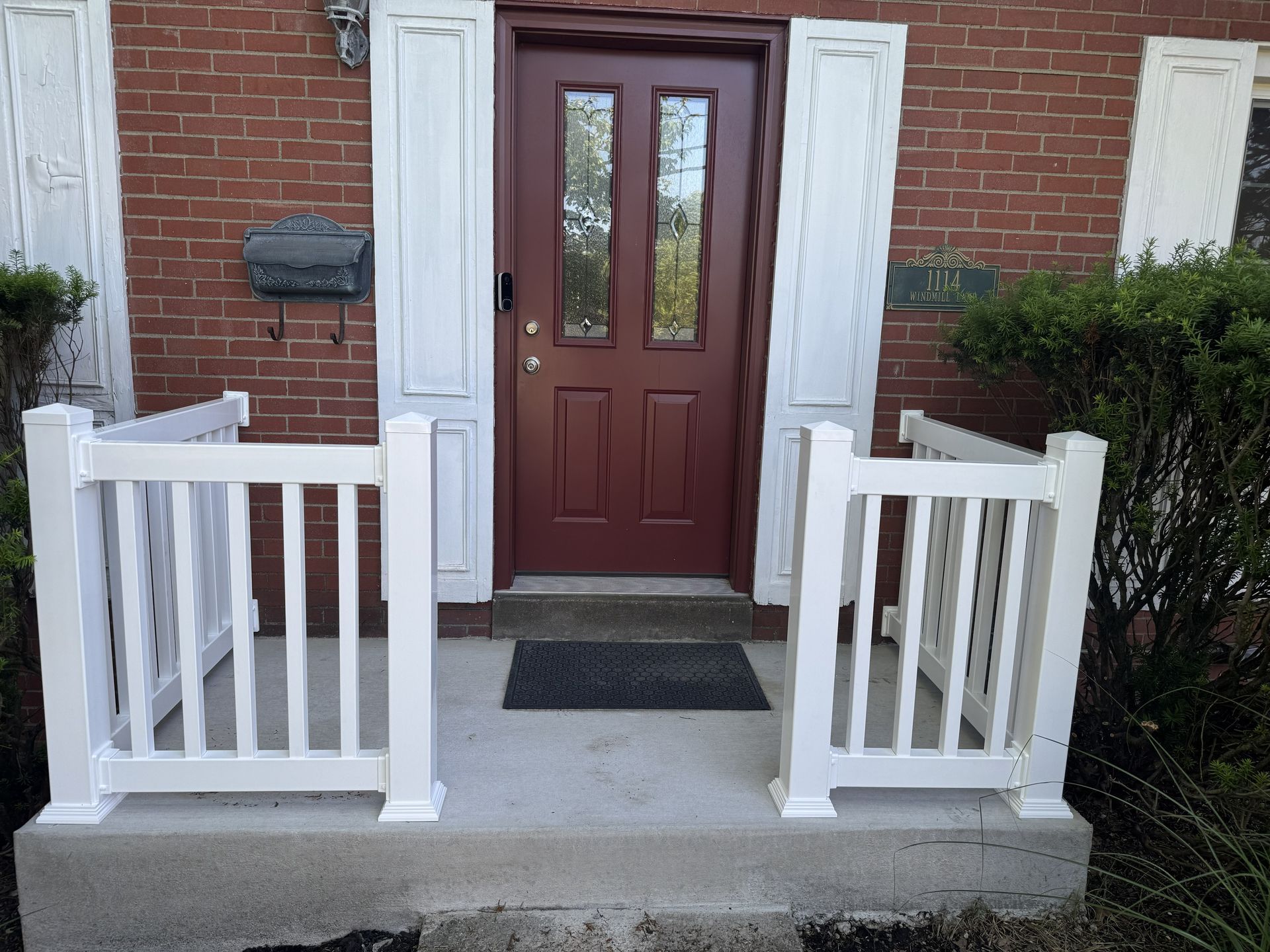 Front porch with a red door, white railings, and brick exterior.