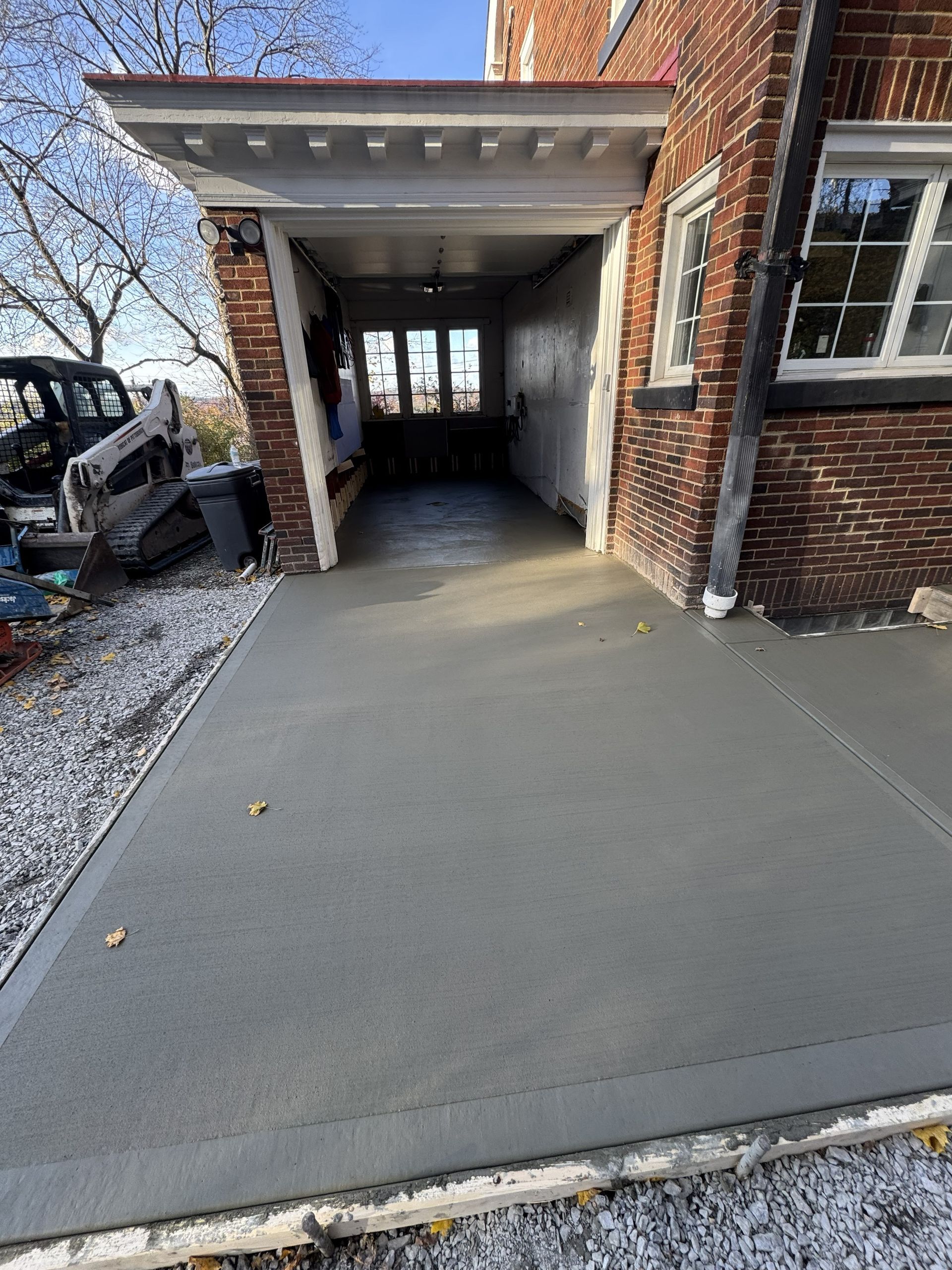 Concrete driveway leading to a covered brick carport beside a house, with a vehicle parked on the left.