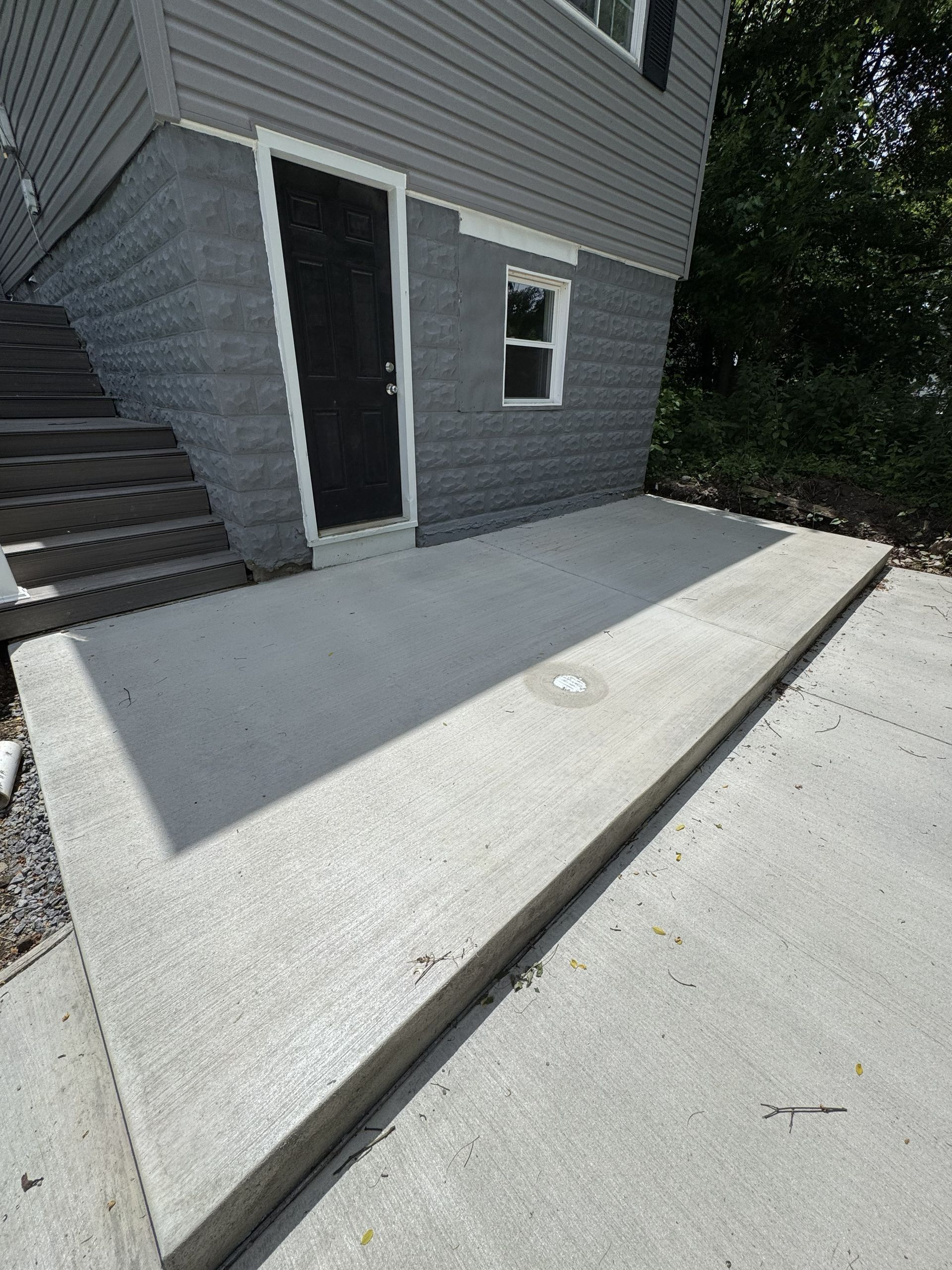 Concrete wheelchair ramp beside gray house with a dark door and stairs