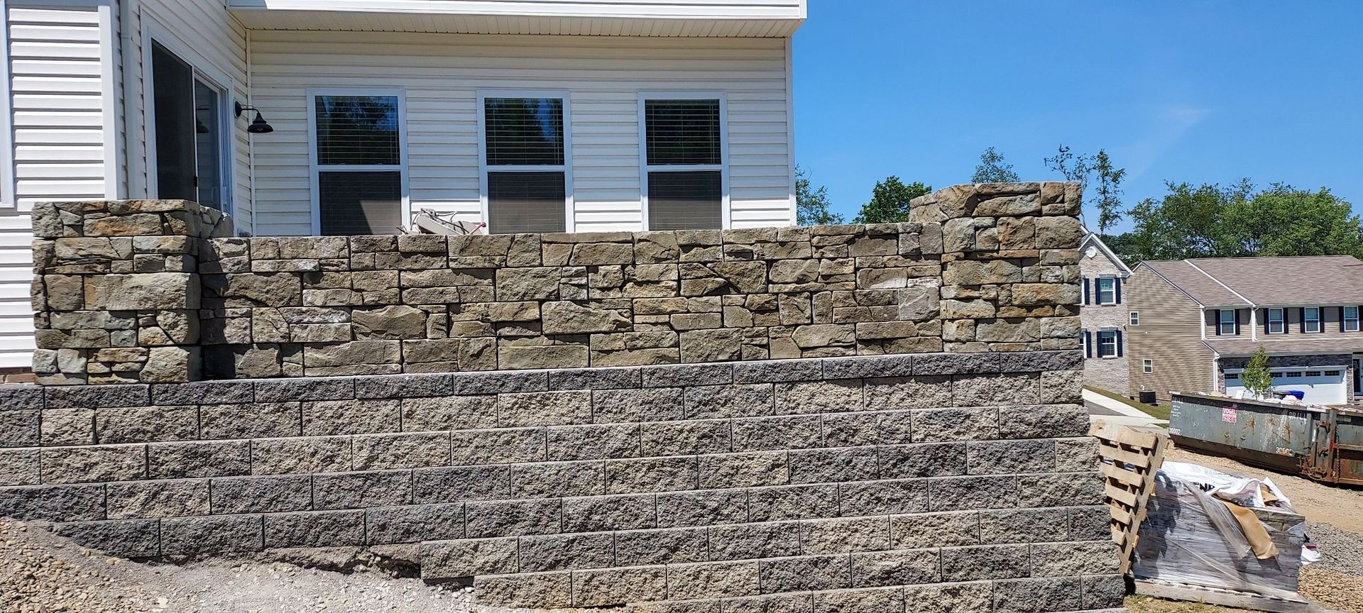 Stone retaining wall in front of a white house under construction on a sunny day