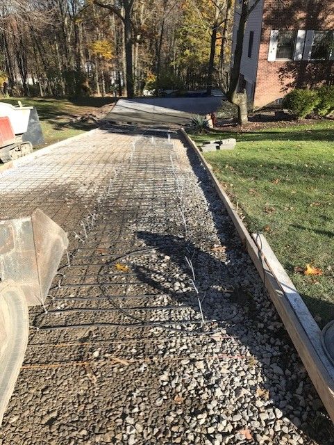 Partially paved driveway with exposed gravel and cracked mesh beside a house and lawn.