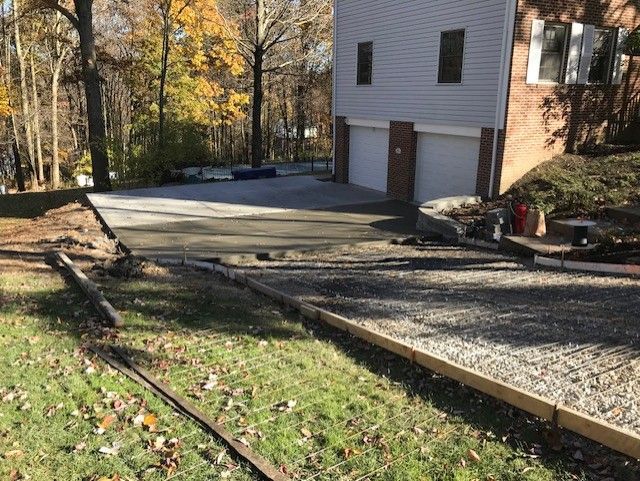 Driveway and gravel area beside a house, with fallen tree branches and a wooded yard in autumn.