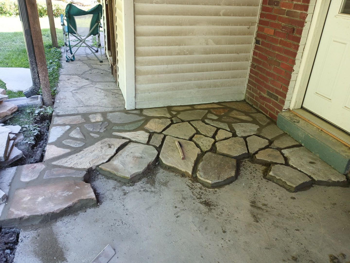 Cracked stone patchwork on a front porch beside a beige door and brick wall
