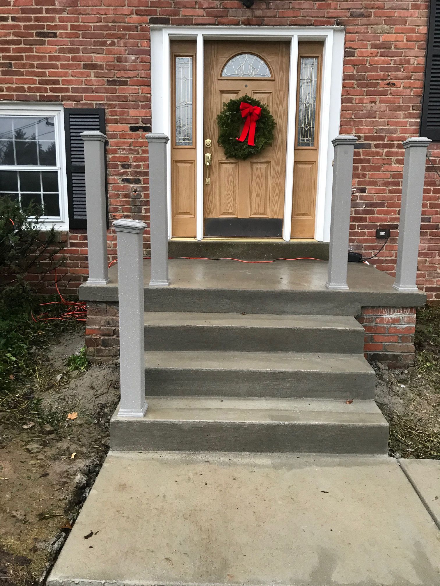 Front steps leading to a brick house entrance with a boarded door and a holiday wreath.