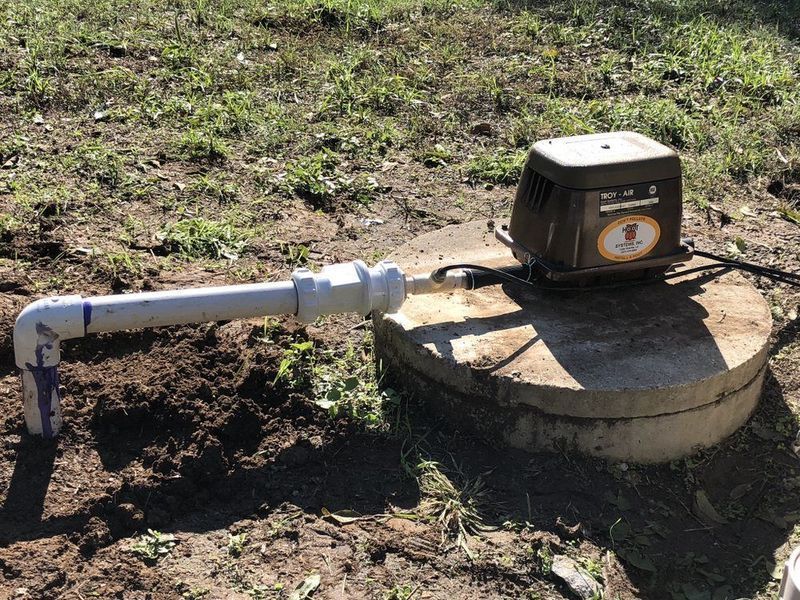 Well pump system with a gray concrete base, beige pump, and white PVC piping.