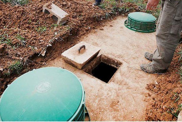Man beside open septic tank access. Green lids and concrete surface, dirt and grass visible.