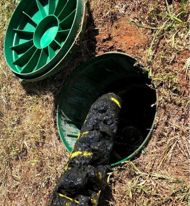 Open septic tank lid with black sludge overflowing. Green lid and surrounding grass visible.