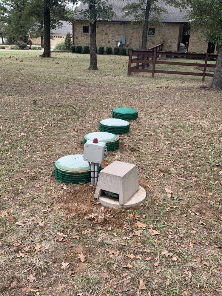Septic system components in a grassy yard, including several green lids, a control box, and concrete structures.