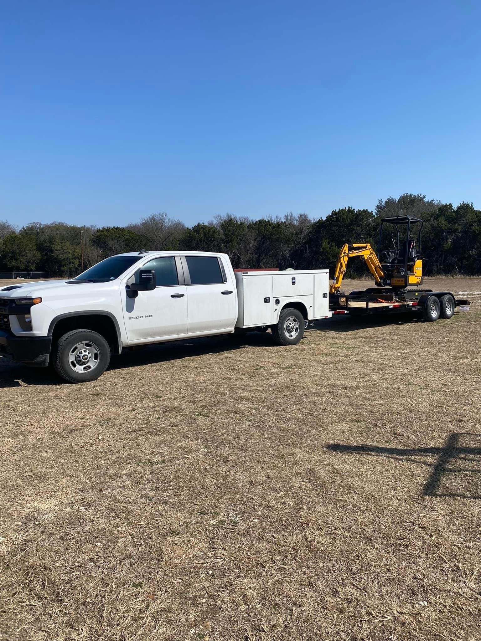 White truck towing a trailer with a small excavator on a field, sunny day.