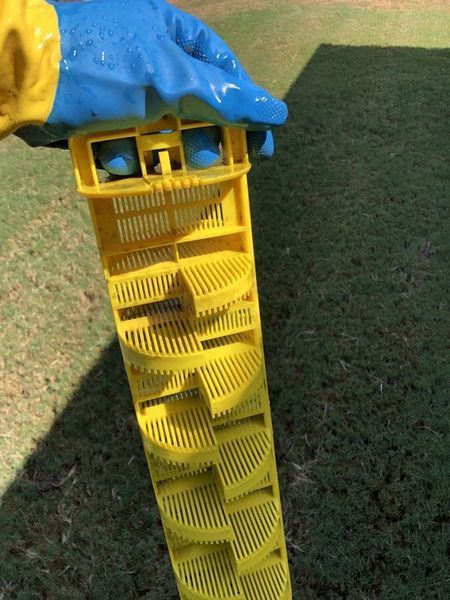 Yellow plastic filter held by a gloved hand, outdoors on grass.