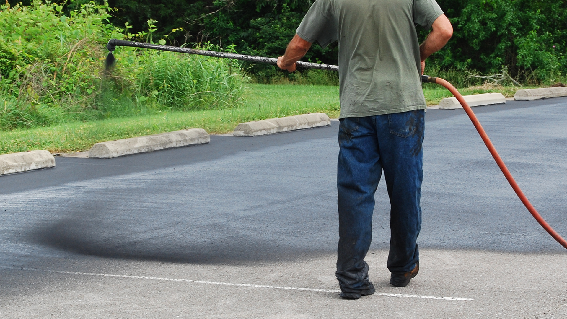 Person spraying water onto a paved road with a hose near a grassy curb