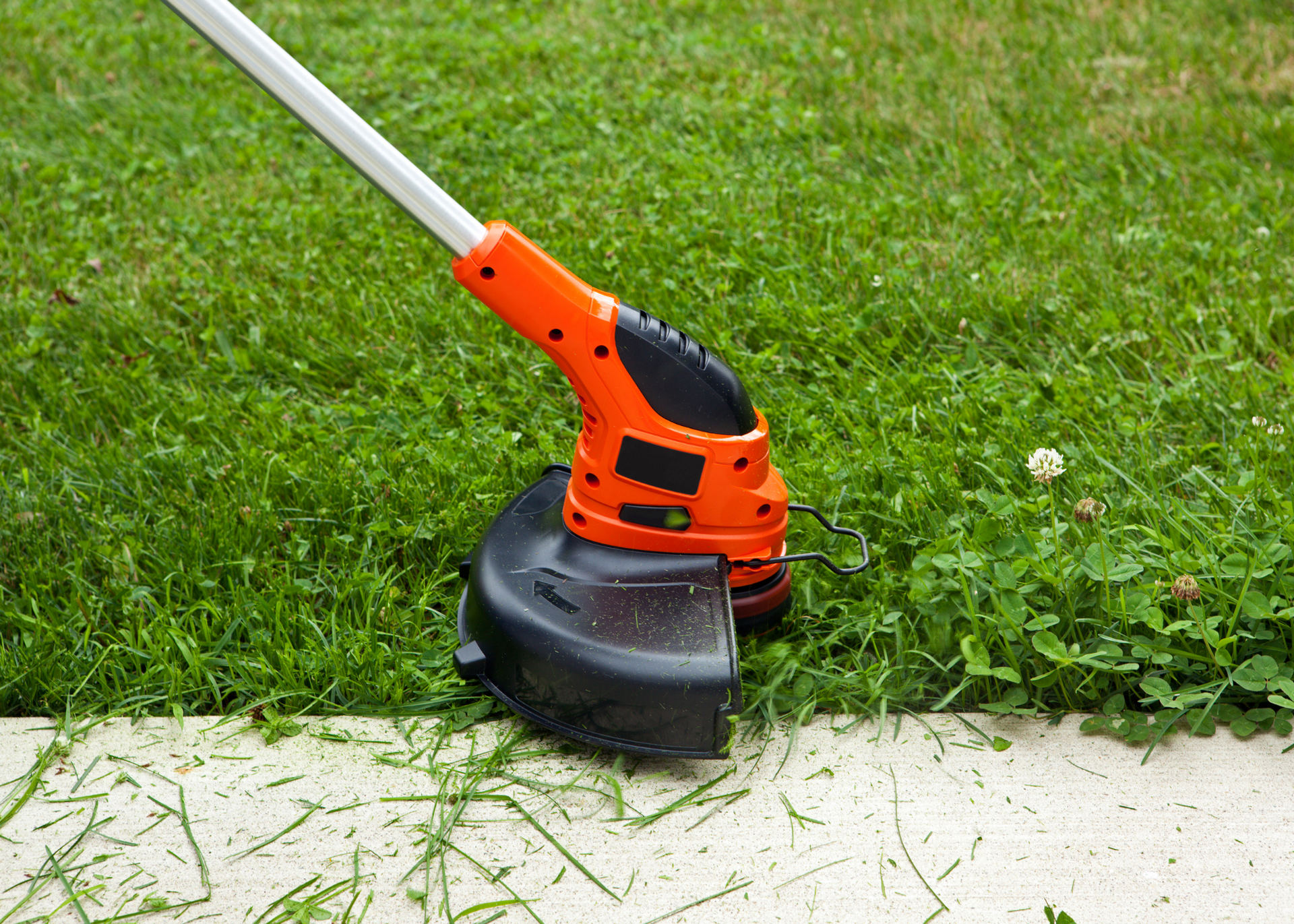 Orange string trimmer on grass beside a concrete edge
