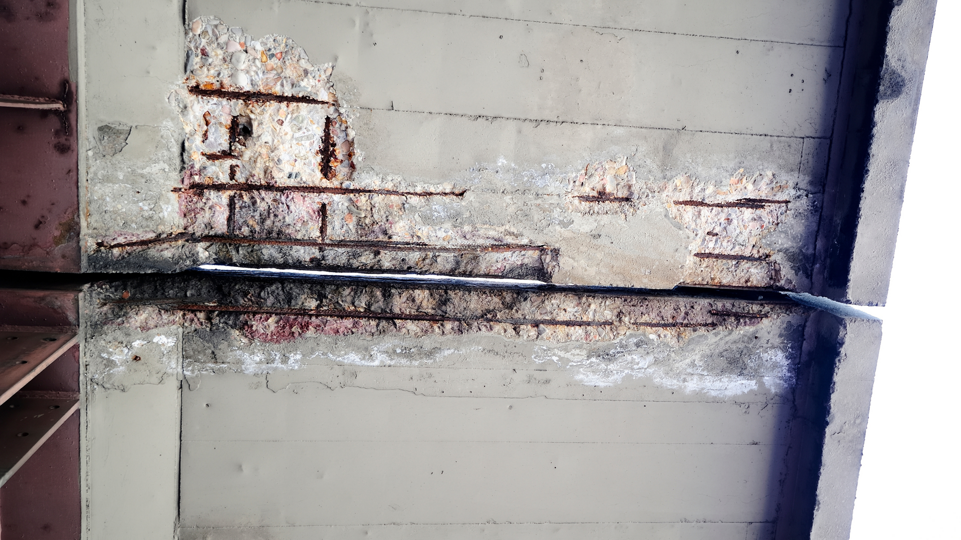 Rust-stained concrete wall with peeling paint and a metal beam or pipe running across it