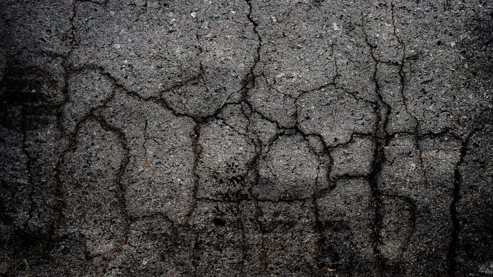 Close-up of cracked gray asphalt with a rough, weathered texture and dark edges