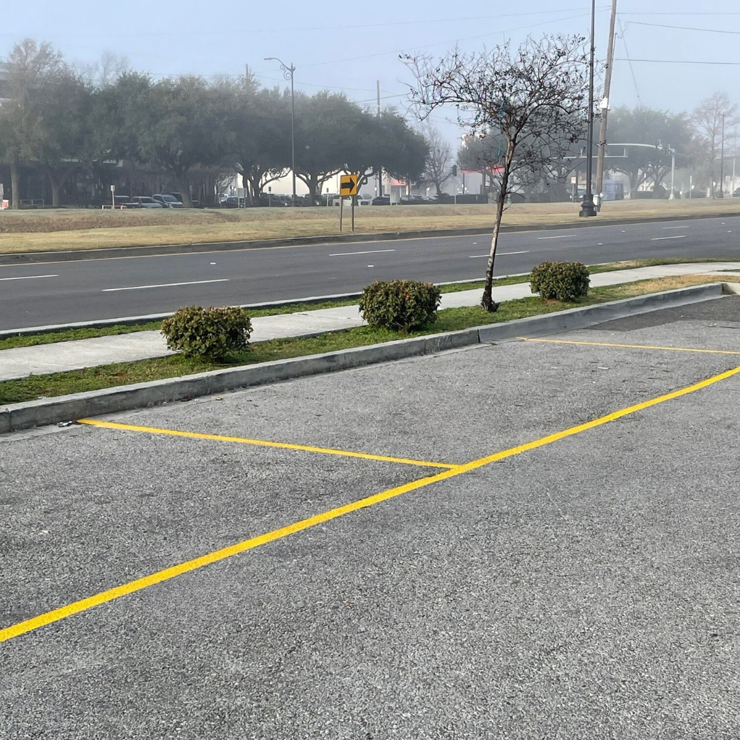 Empty parking lot with yellow lines beside a road, low shrubs, and a foggy background.