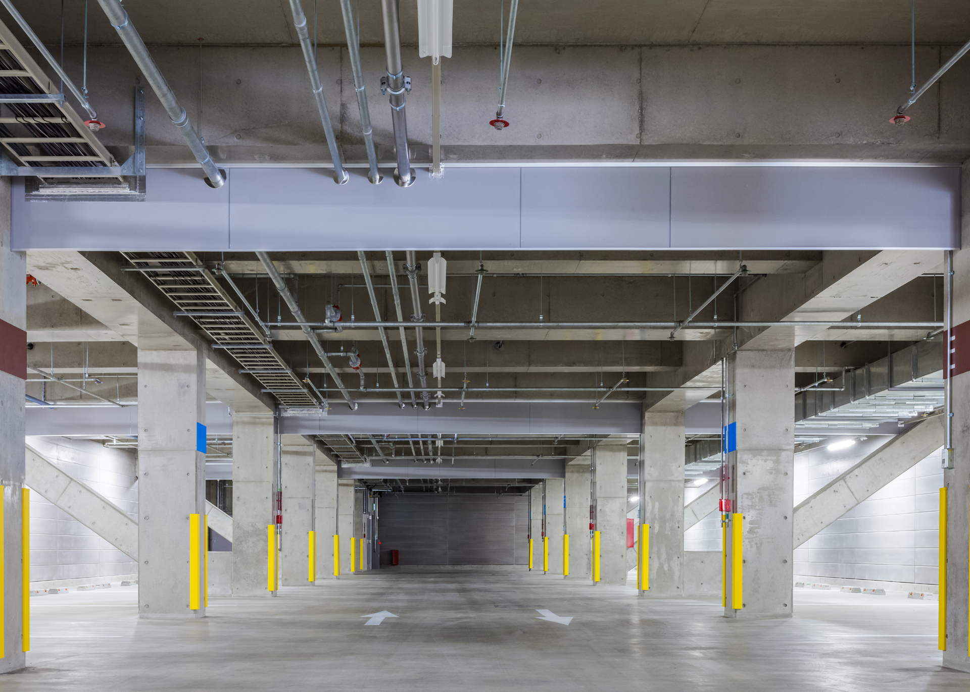 Empty underground parking garage with concrete pillars, yellow safety bollards, and a central lane.