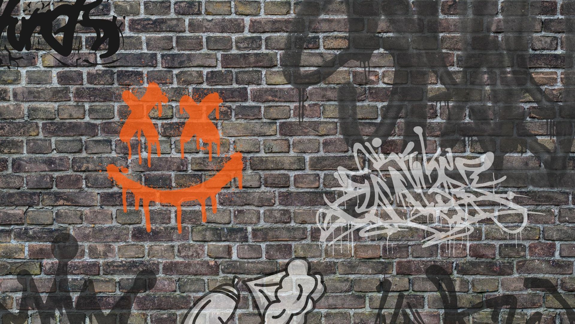 Orange smiley graffiti with X eyes on a gray brick wall, surrounded by white tags and black spray paint.