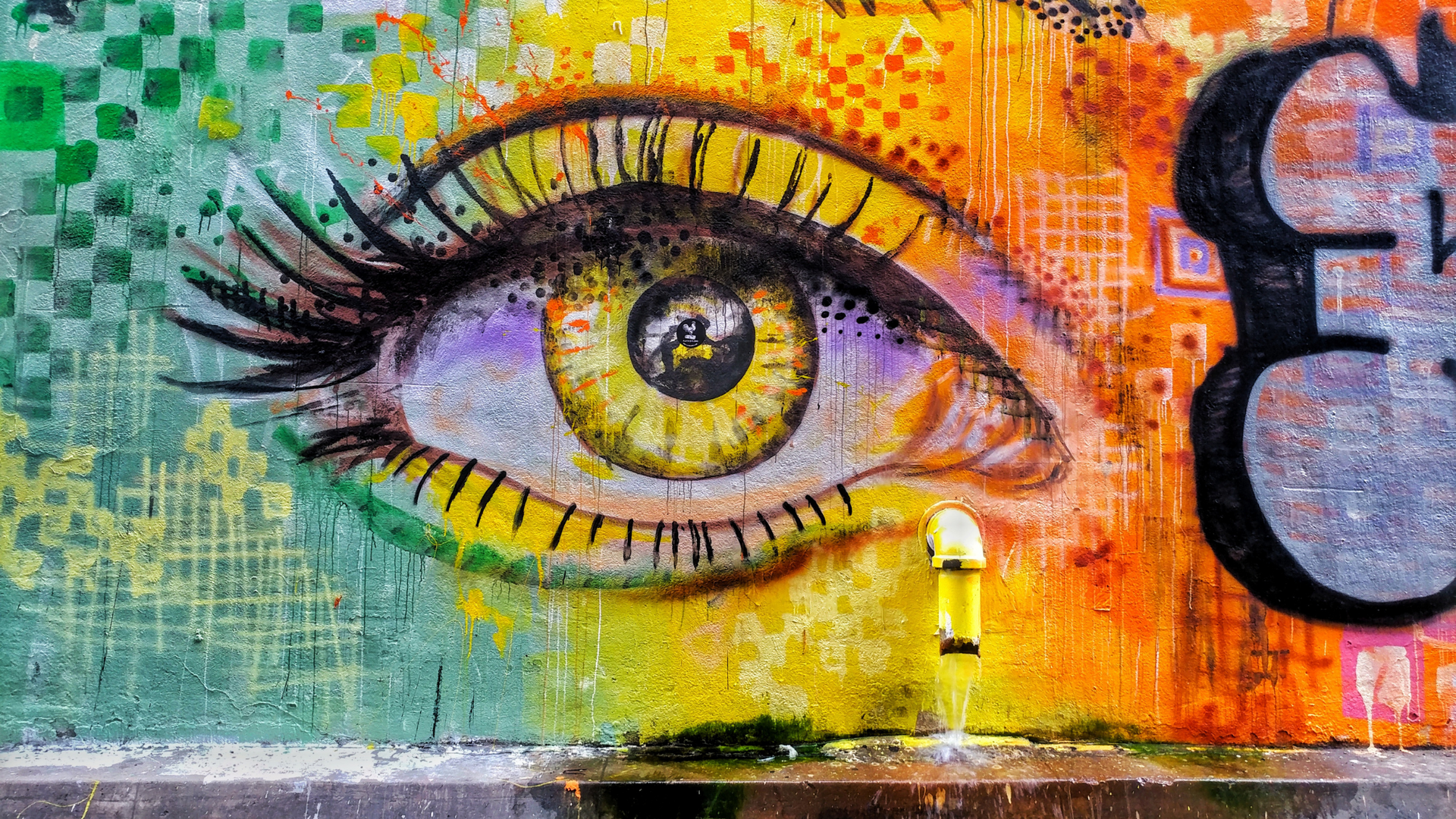 Colorful mural of a large eye on a textured wall with orange, yellow, green, and black graffiti elements