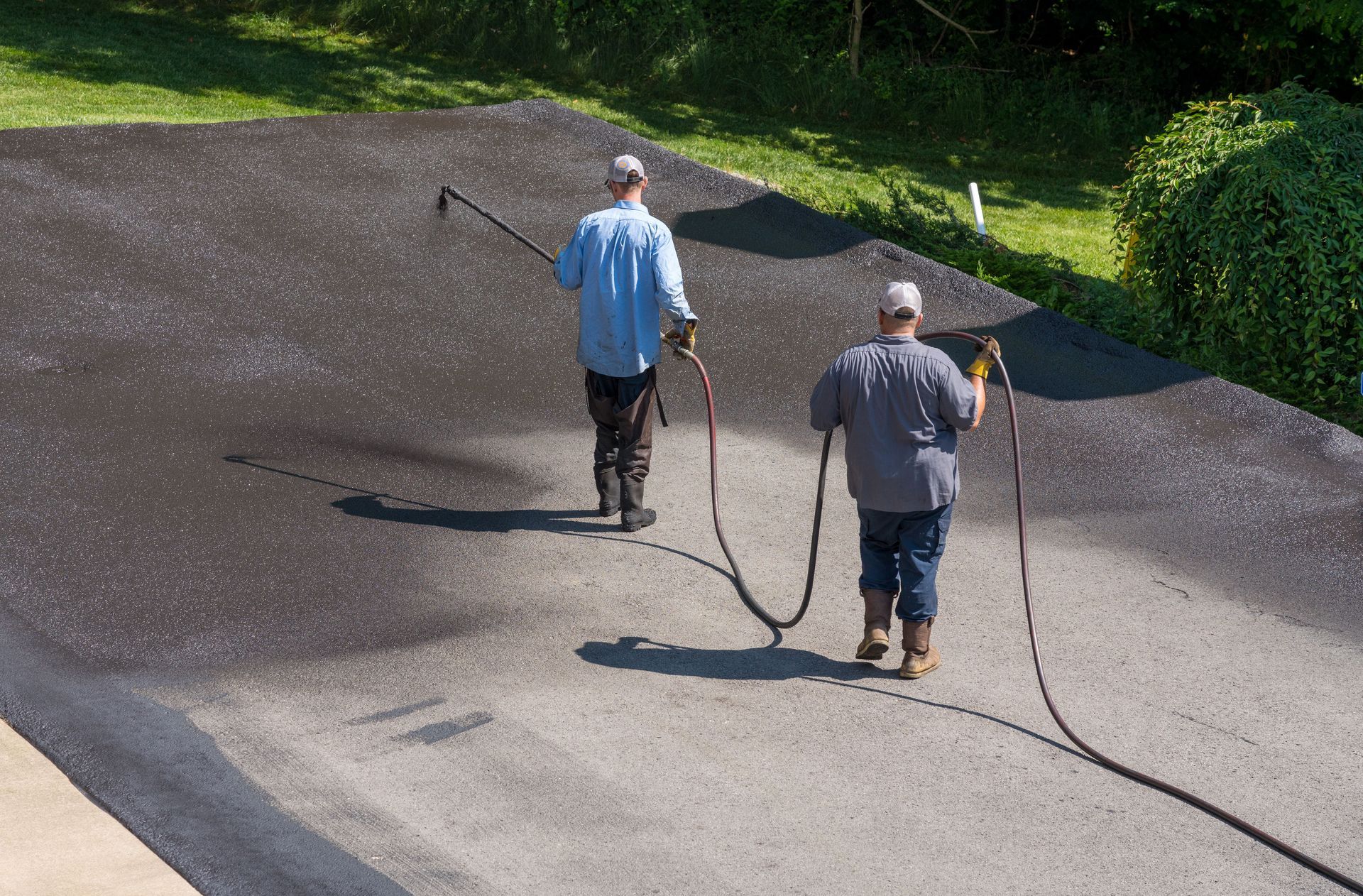 Person using a squeegee to spread dark liquid on a concrete surface outdoors