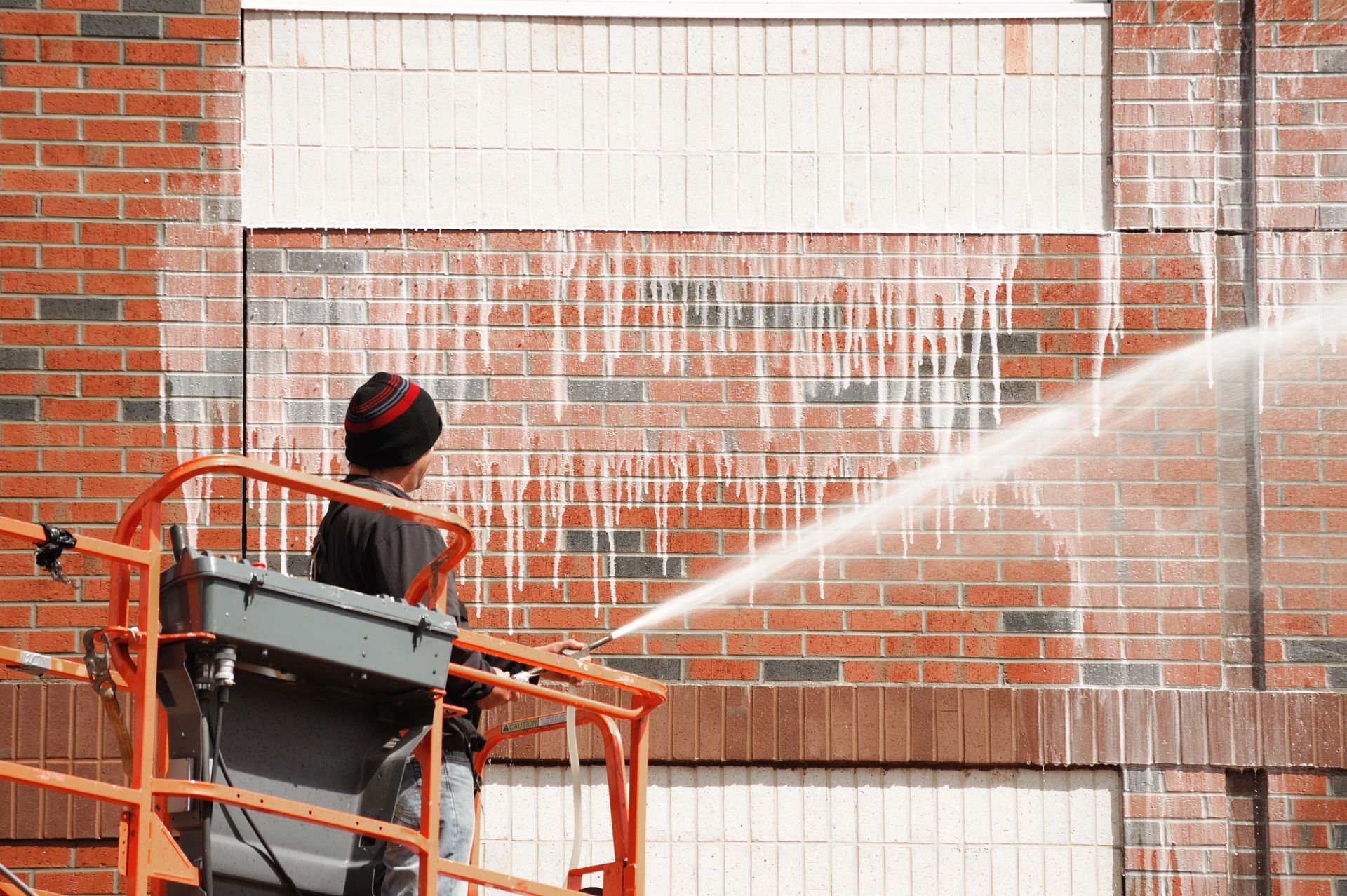 Worker in an orange lift spraying water on a brick wall during cleanup