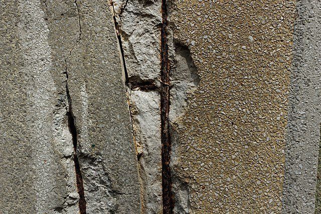 Close-up of a cracked concrete wall with peeling gray and tan surfaces