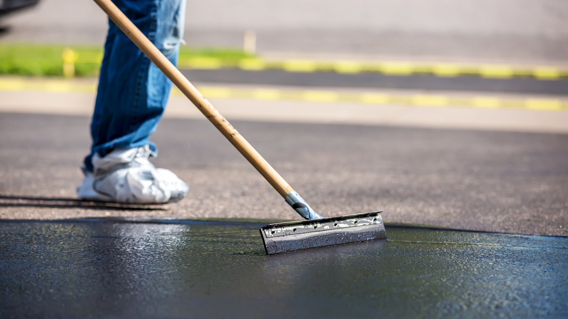 Person painting dark asphalt with a roller near a curb