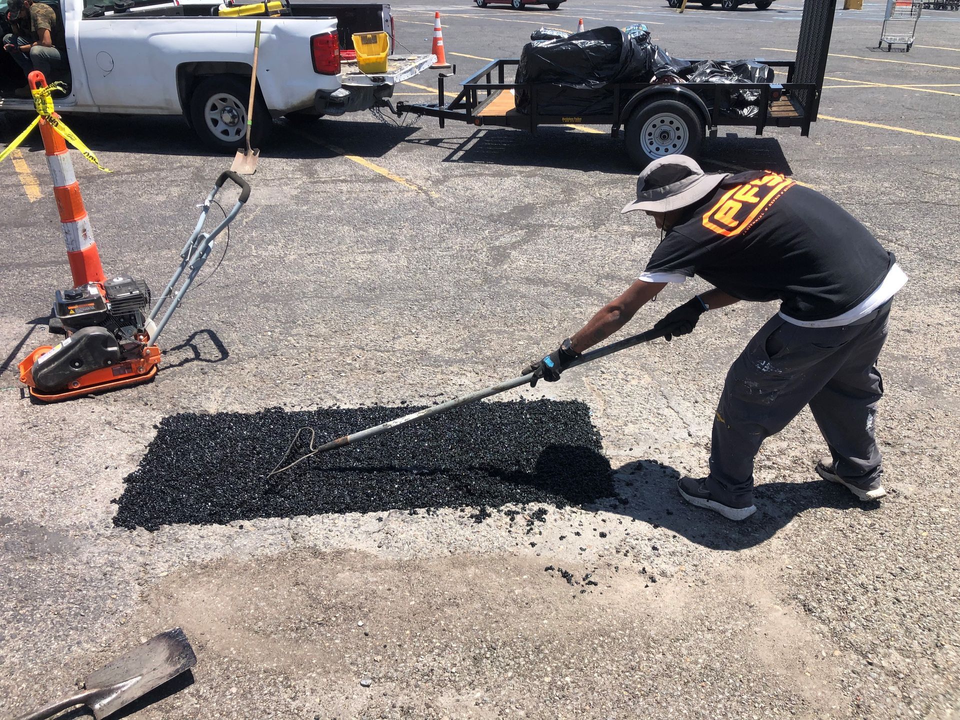 Worker spreads fresh asphalt beside construction equipment on a road repair site.