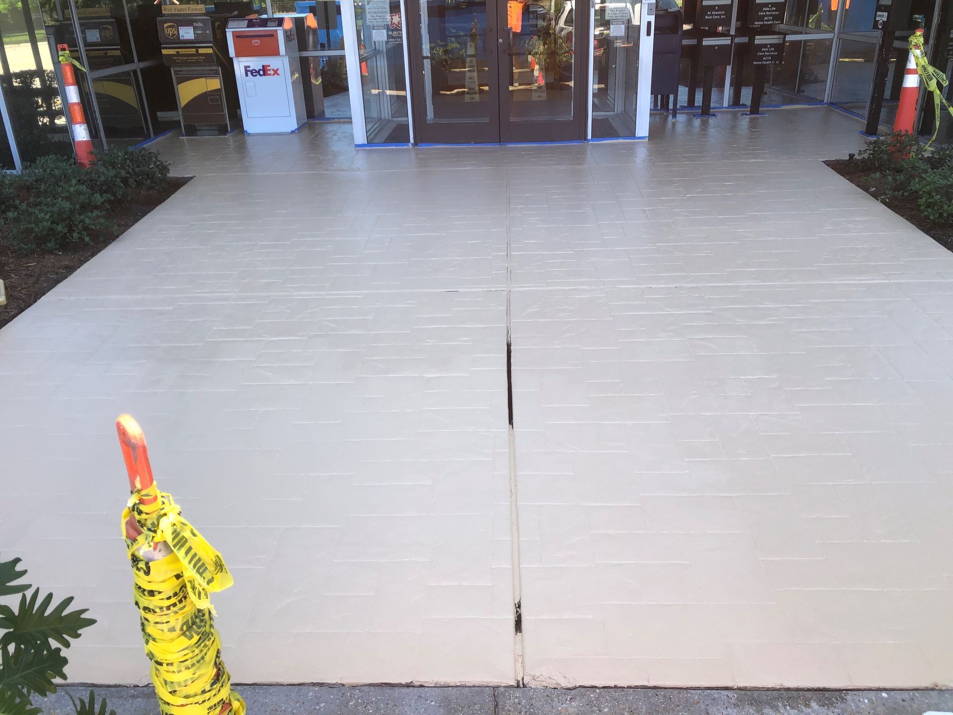 Wide light-gray walkway leading to a storefront entrance, with a yellow post in the foreground.