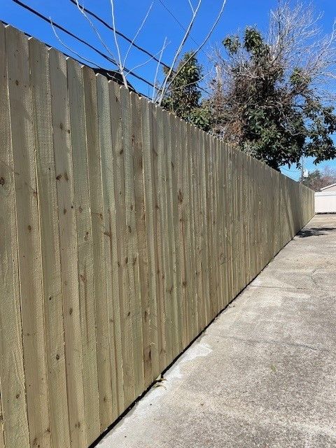 Wooden privacy fence along a concrete walkway under a clear blue sky