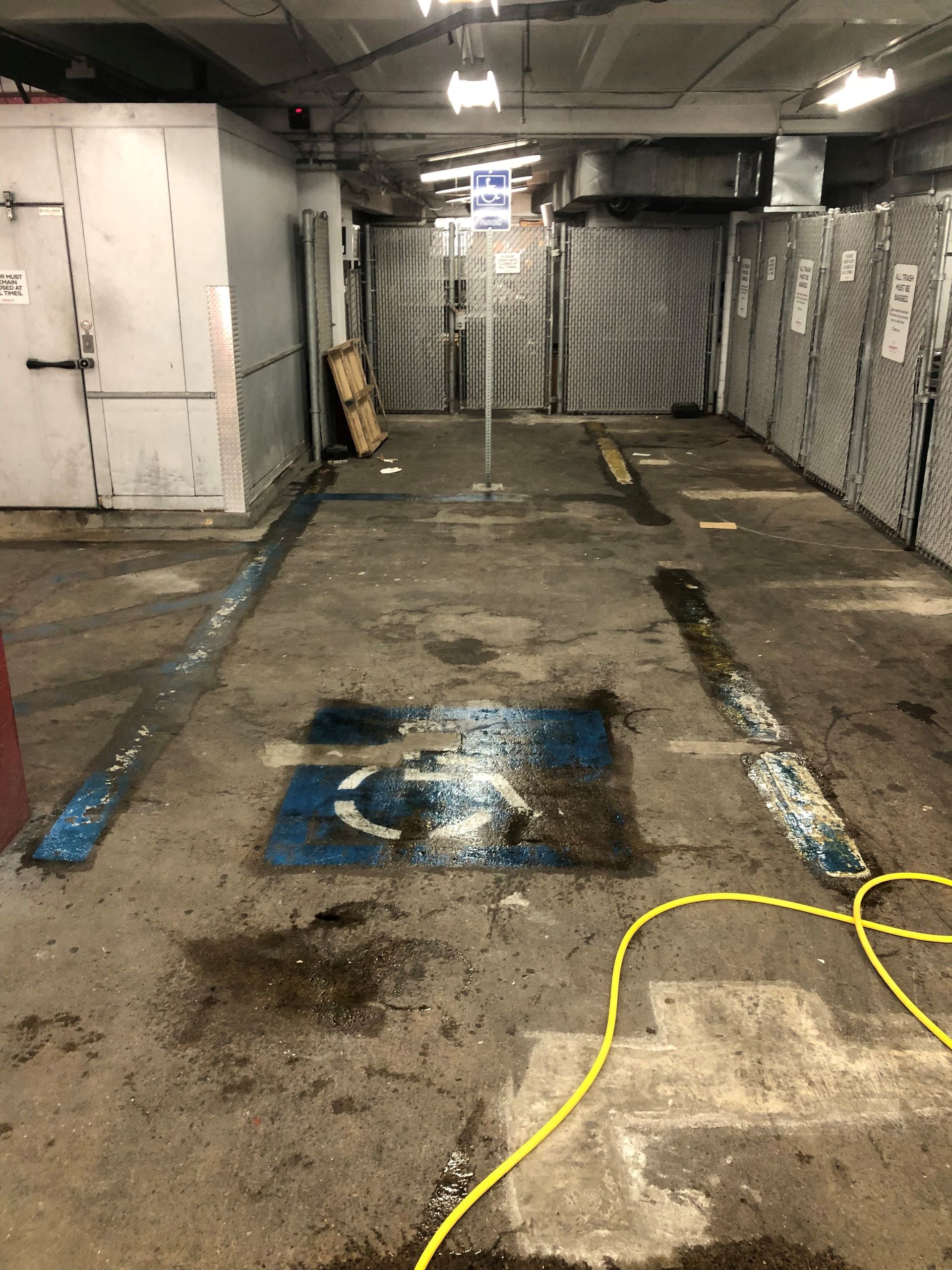Dim industrial parking garage with stained concrete, metal walls, and yellow cords on the floor