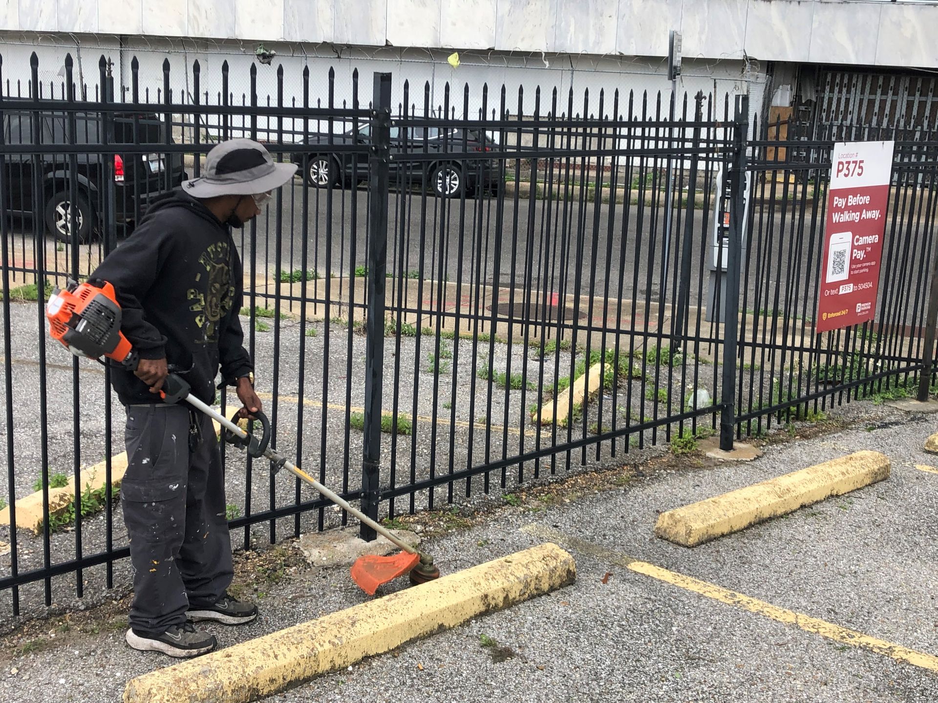 Person using a leaf blower near a black fence and curb in a parking lot