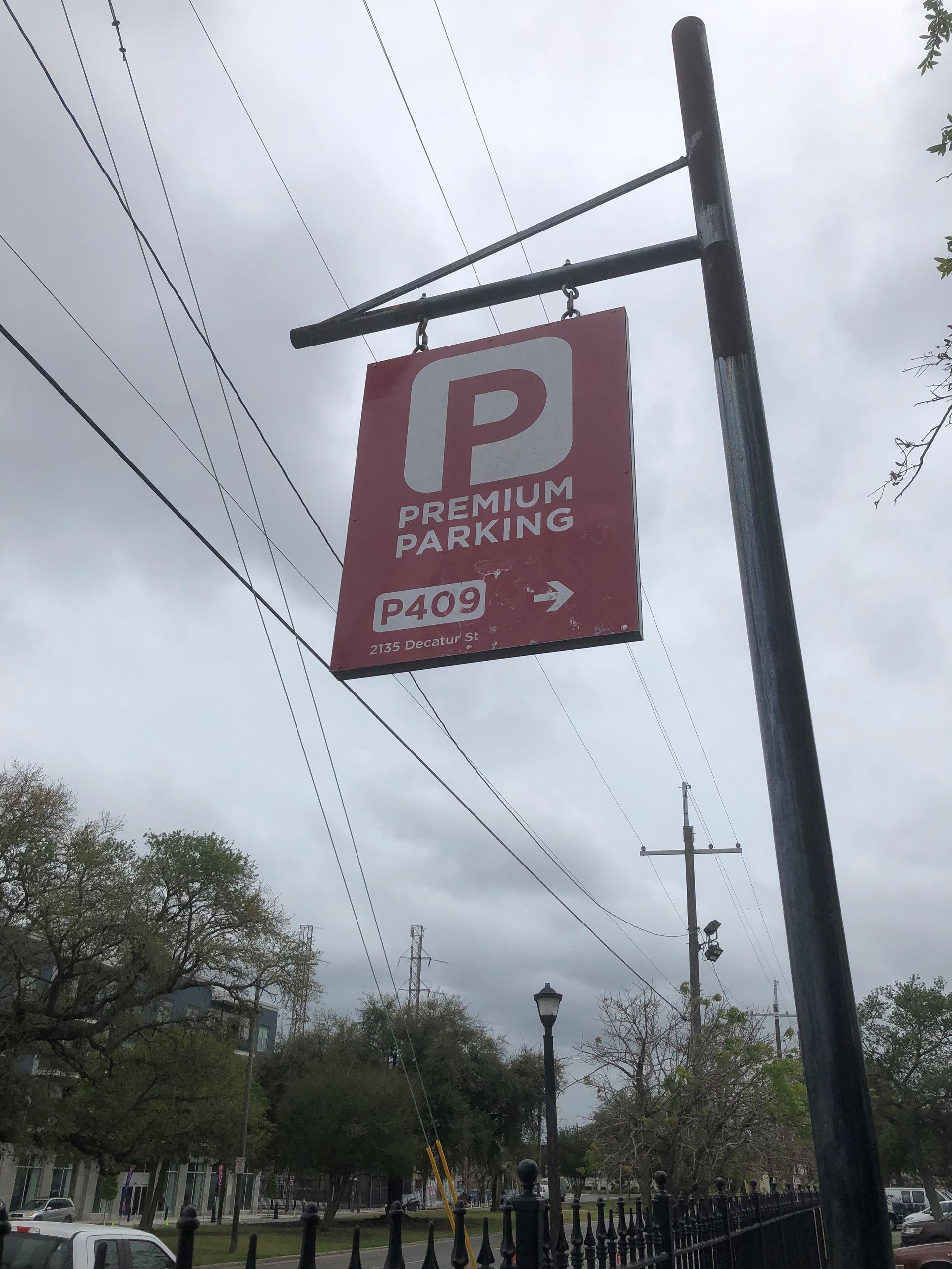 Red premium parking sign with white “P” on a pole beside a street, under cloudy skies.