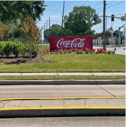 Coca-Cola sign in a landscaped median beside a street with traffic lights and trees