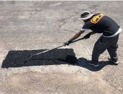 Worker paving a patch in a cracked asphalt road with a squeegee