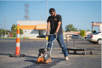 Worker using a jackhammer to break pavement in a parking lot under a clear sky
